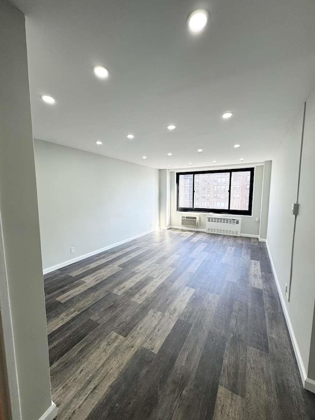 empty room featuring baseboards, dark wood-type flooring, radiator heating unit, and recessed lighting