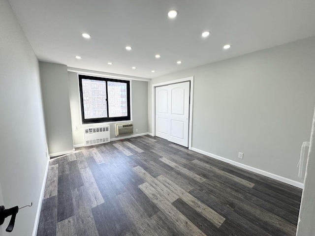 unfurnished room with dark wood-style floors, a wall unit AC, recessed lighting, radiator heating unit, and baseboards