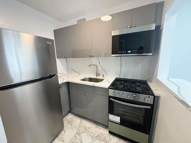 kitchen with stainless steel appliances, a sink, marble finish floor, gray cabinets, and decorative backsplash