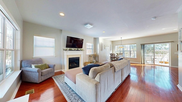 living room with recessed lighting, dark wood-style flooring, visible vents, baseboards, and a glass covered fireplace