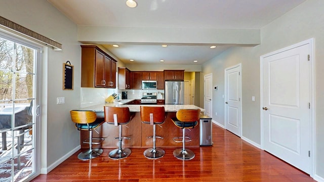 kitchen featuring a peninsula, a breakfast bar, dark wood-style flooring, appliances with stainless steel finishes, and decorative backsplash