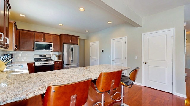 kitchen featuring light stone counters, dark wood-style floors, a breakfast bar area, backsplash, and appliances with stainless steel finishes