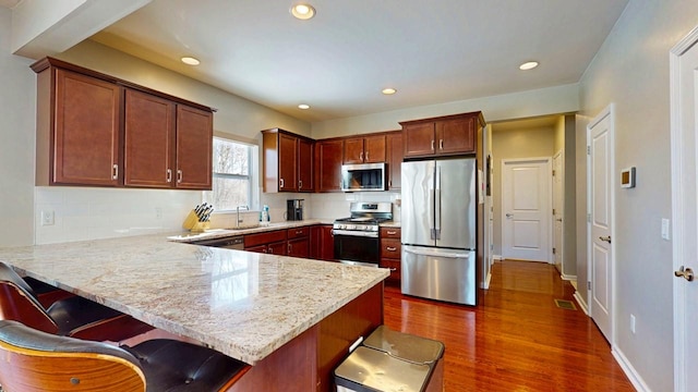 kitchen featuring dark wood finished floors, appliances with stainless steel finishes, a breakfast bar, light stone countertops, and recessed lighting