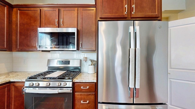 kitchen featuring stainless steel appliances, light stone counters, and tasteful backsplash