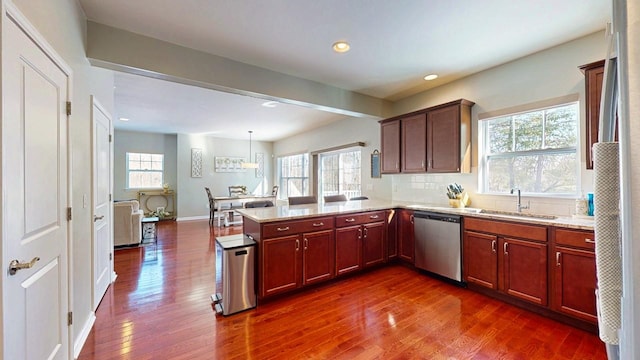 kitchen with pendant lighting, dark wood finished floors, a sink, dishwasher, and a peninsula