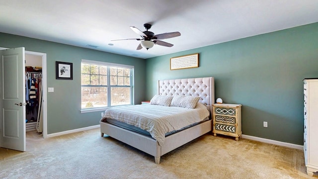 bedroom featuring a ceiling fan, a walk in closet, light colored carpet, and baseboards