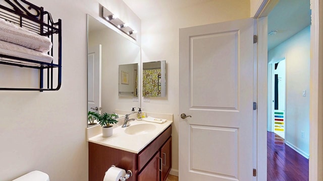 half bathroom featuring toilet, baseboards, wood finished floors, and vanity