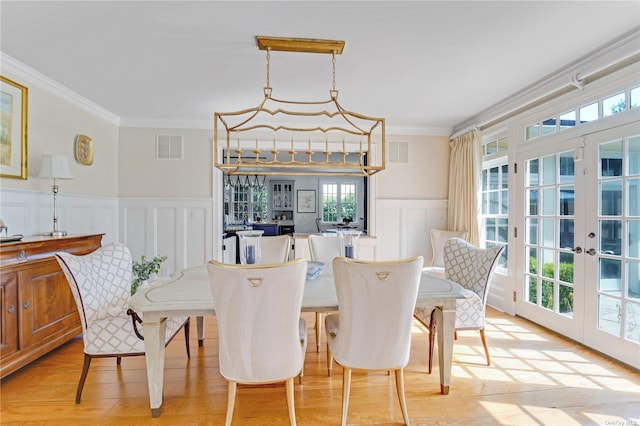 dining space with crown molding, light wood-type flooring, and french doors