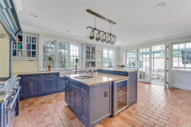 kitchen featuring an island with sink, sink, pendant lighting, and beverage cooler