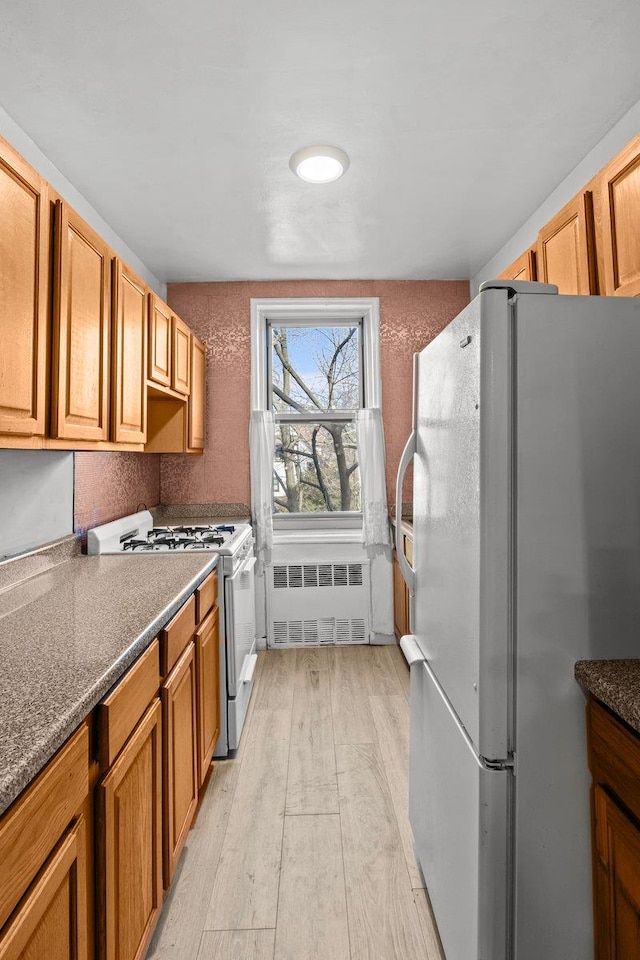 kitchen featuring white appliances, radiator heating unit, and light hardwood / wood-style flooring