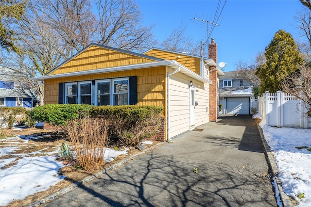 view of front of home featuring an outbuilding, driveway, a chimney, and fence