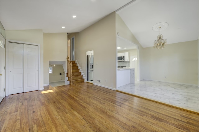 unfurnished living room featuring light wood-type flooring, a notable chandelier, baseboards, and stairs