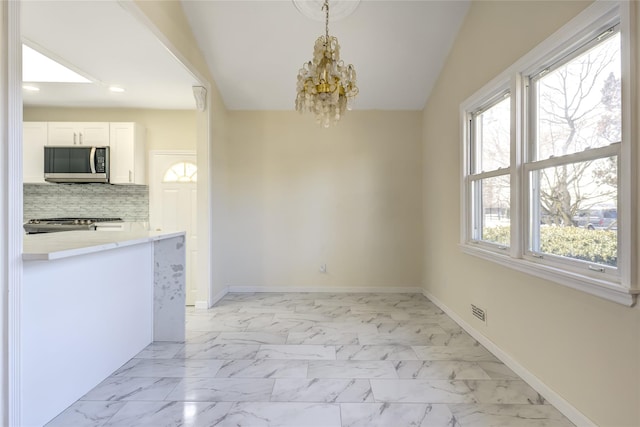 unfurnished dining area featuring marble finish floor, visible vents, a notable chandelier, and baseboards