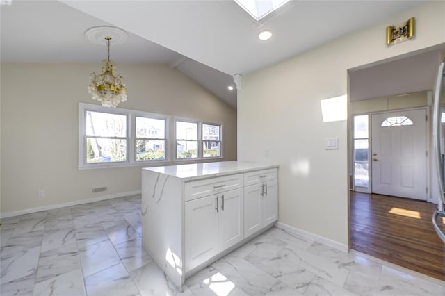 kitchen featuring a peninsula, marble finish floor, white cabinetry, and lofted ceiling with skylight