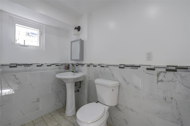 bathroom with wainscoting, toilet, and tile walls