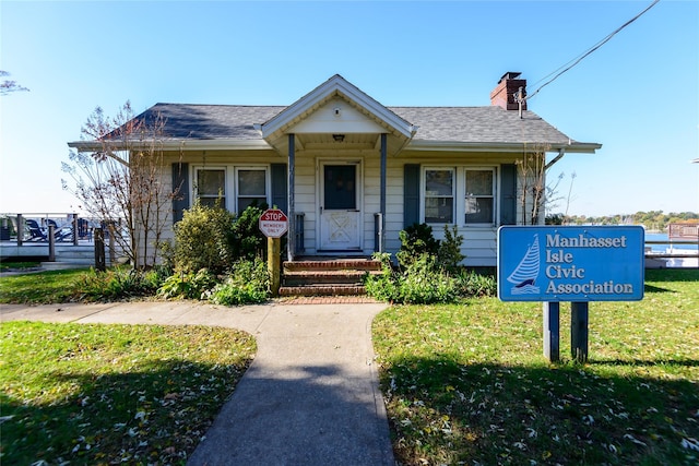 bungalow-style house featuring roof with shingles, a chimney, and a front yard