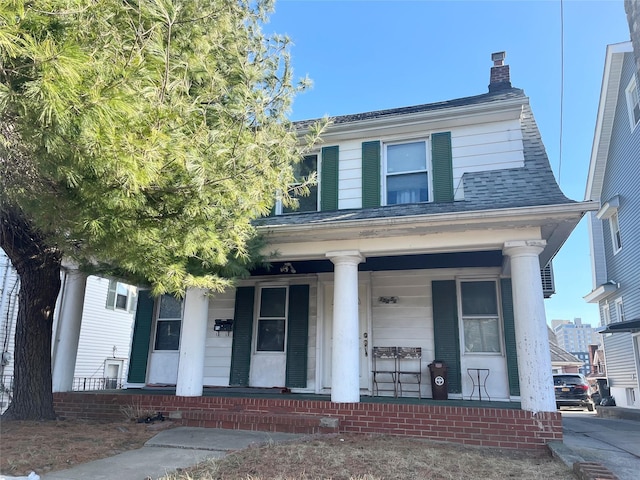 view of front of house with a chimney, a porch, and a shingled roof