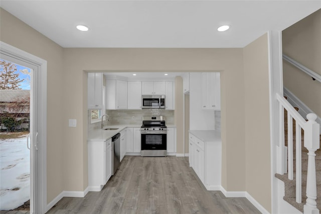 kitchen with stainless steel appliances, white cabinets, backsplash, sink, and light wood-type flooring