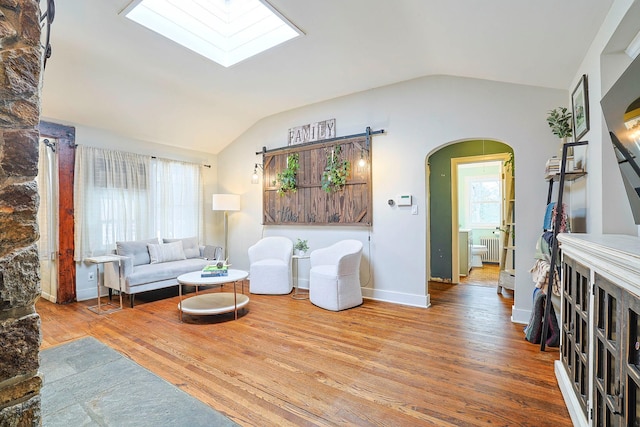 living room with wood-type flooring, vaulted ceiling with skylight, and radiator