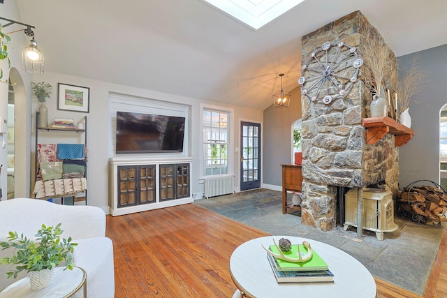 living room featuring radiator, hardwood / wood-style floors, vaulted ceiling with skylight, a notable chandelier, and a fireplace