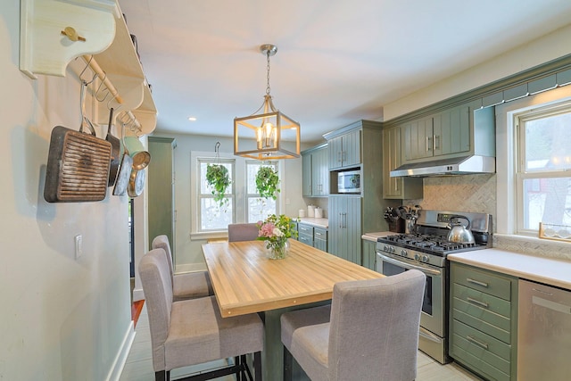 kitchen featuring appliances with stainless steel finishes, tasteful backsplash, a healthy amount of sunlight, green cabinetry, and decorative light fixtures