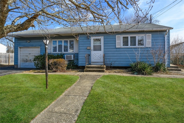 single story home featuring a front lawn, an attached garage, a wall unit AC, and aphalt driveway