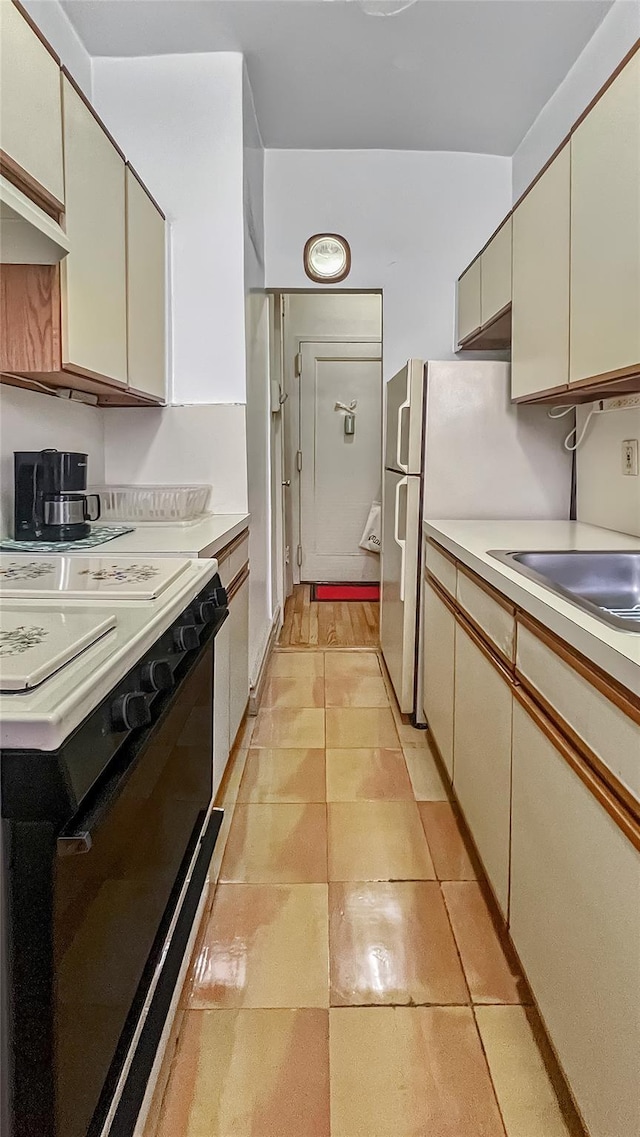 kitchen featuring cream cabinets, black range, sink, and light tile patterned flooring