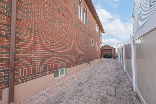 view of side of property featuring brick siding, a detached garage, a patio area, fence, and driveway