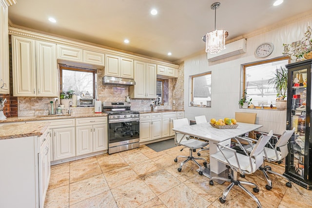 kitchen with hanging light fixtures, an AC wall unit, stainless steel range with gas stovetop, a sink, and under cabinet range hood