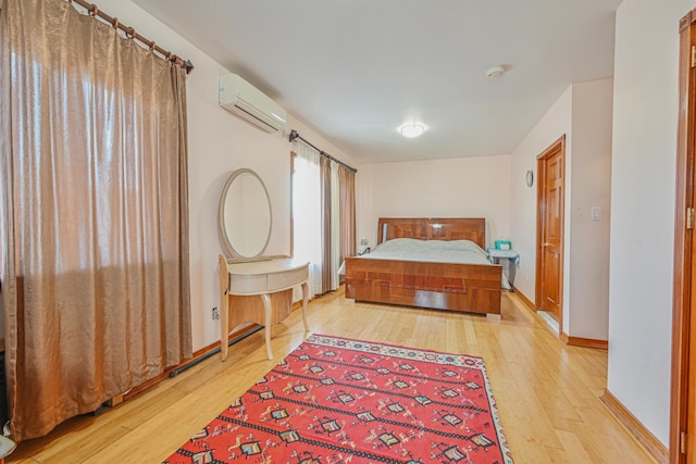 bedroom featuring light wood-type flooring, baseboards, and a wall mounted air conditioner