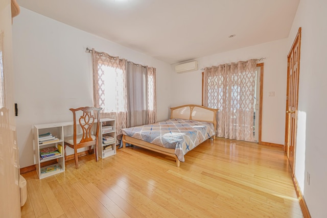 bedroom featuring an AC wall unit, wood finished floors, and baseboards