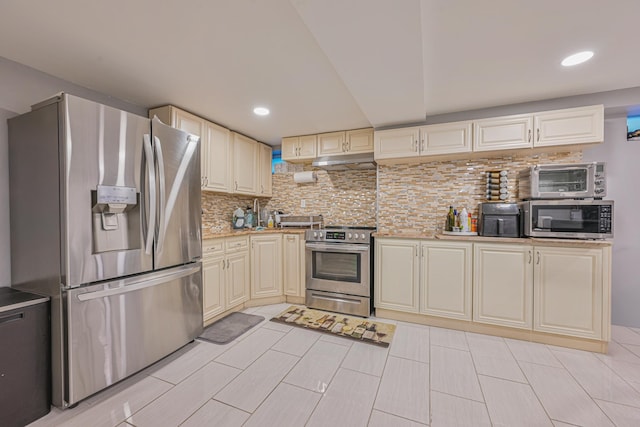 kitchen featuring under cabinet range hood, stainless steel appliances, light countertops, cream cabinetry, and decorative backsplash