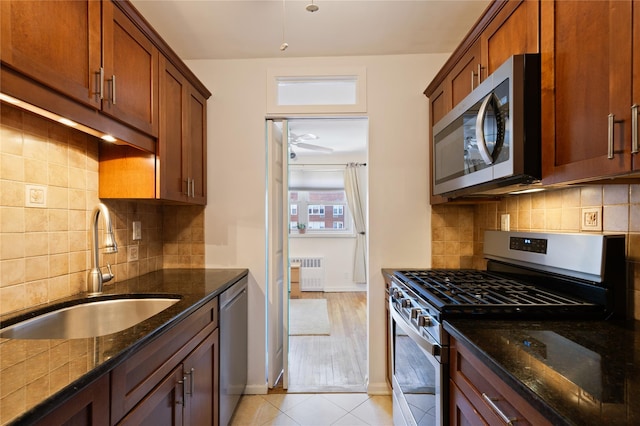 kitchen with stainless steel appliances, backsplash, radiator heating unit, a sink, and dark stone counters