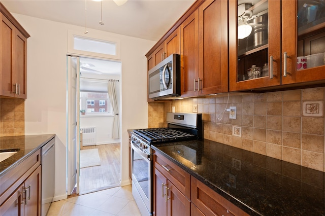 kitchen featuring appliances with stainless steel finishes, radiator, dark stone counters, tasteful backsplash, and brown cabinetry