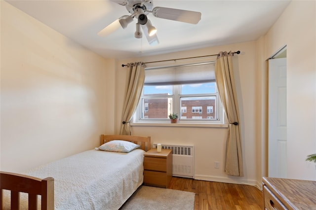 bedroom featuring ceiling fan, radiator heating unit, wood finished floors, and baseboards