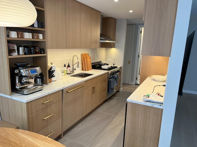 kitchen with light brown cabinetry, sink, backsplash, high end range, and light stone counters