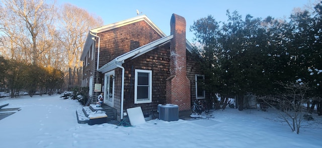 view of snowy exterior featuring central AC unit and a chimney