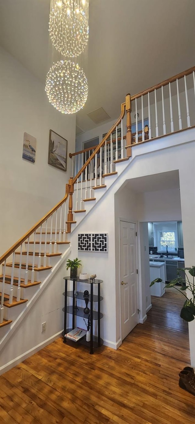 staircase with a high ceiling, baseboards, wood-type flooring, and a chandelier