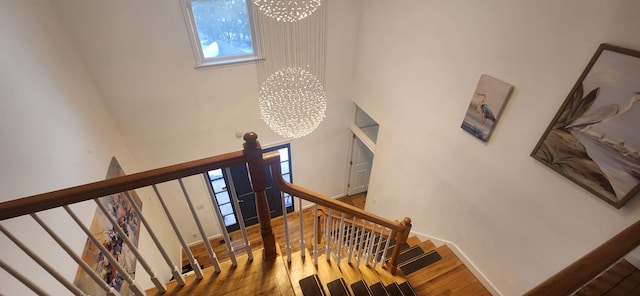 stairway with a chandelier, a towering ceiling, and wood finished floors