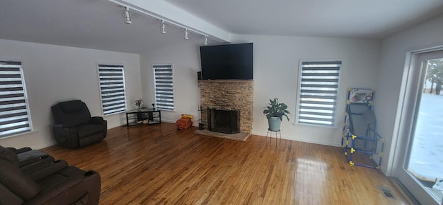 living room with a wealth of natural light, visible vents, a stone fireplace, and light wood-type flooring