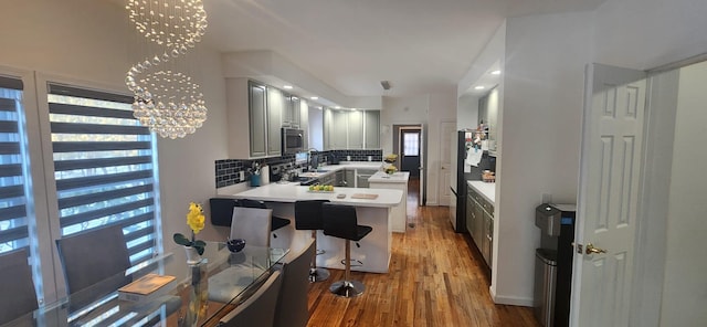 kitchen featuring a notable chandelier, backsplash, wood finished floors, appliances with stainless steel finishes, and a peninsula