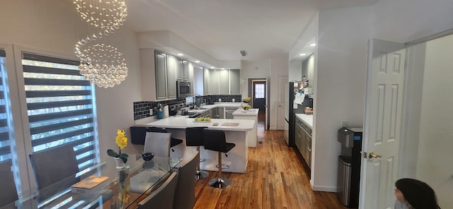 kitchen featuring light wood-type flooring, backsplash, stainless steel appliances, a peninsula, and a chandelier