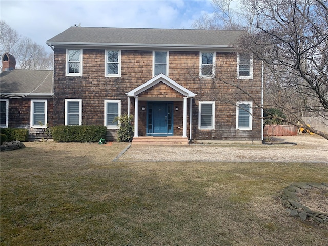 colonial house featuring a front yard and a shingled roof