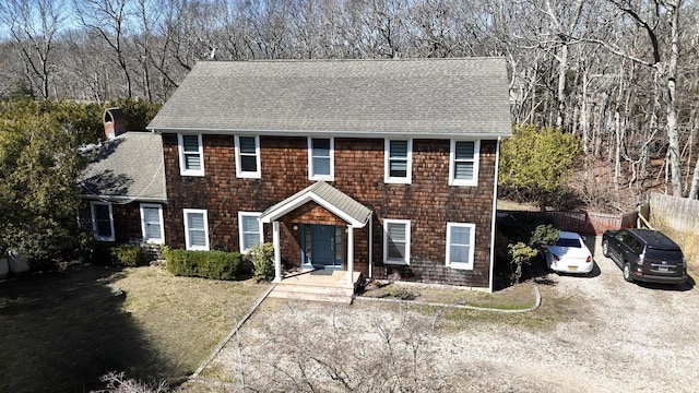 colonial home featuring a shingled roof, fence, and a front yard