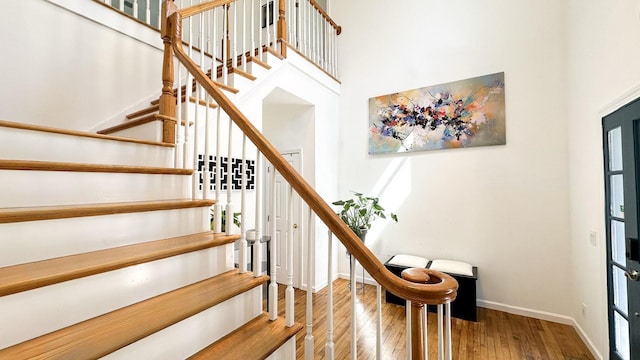 stairway featuring baseboards, a high ceiling, and wood finished floors