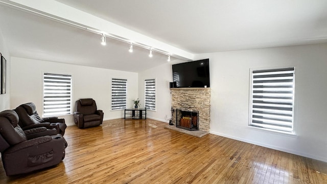living area with vaulted ceiling, light wood finished floors, a fireplace, rail lighting, and baseboards