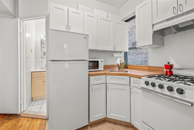 kitchen with light tile patterned flooring, butcher block countertops, white cabinetry, sink, and white appliances