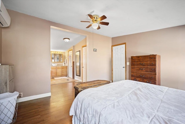 bedroom featuring hardwood / wood-style flooring, ensuite bath, a wall unit AC, and ceiling fan