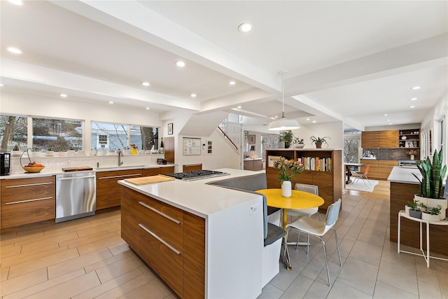 kitchen featuring stainless steel appliances, a kitchen island, sink, beamed ceiling, and pendant lighting