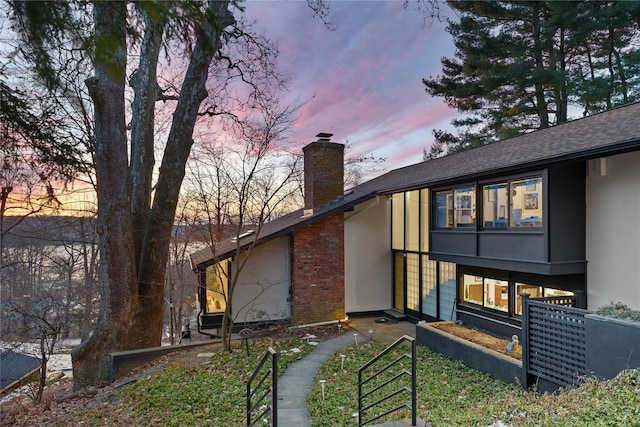 back of house featuring a shingled roof, a chimney, and stucco siding